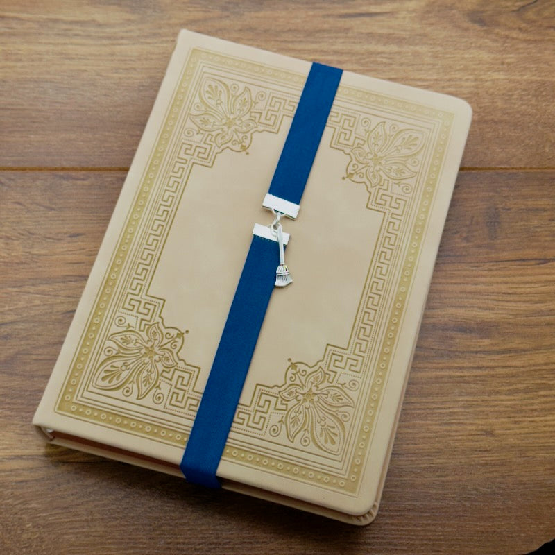 A silver broom charm on an elastic Bookband